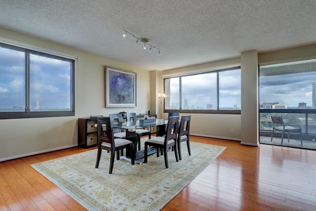 dining space with a textured ceiling, light wood-type flooring, and track lighting