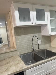 kitchen with decorative backsplash, white cabinetry, sink, and light stone counters