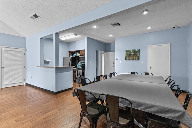 dining room with light hardwood / wood-style floors, lofted ceiling, and a textured ceiling