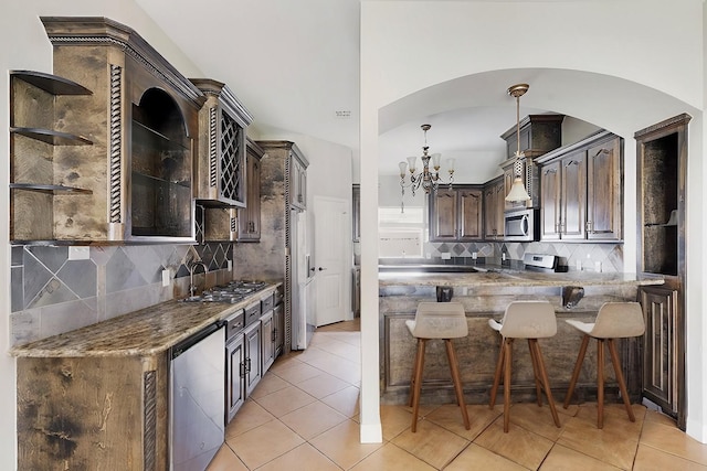 kitchen with a kitchen breakfast bar, light tile patterned floors, tasteful backsplash, dark brown cabinets, and stainless steel appliances