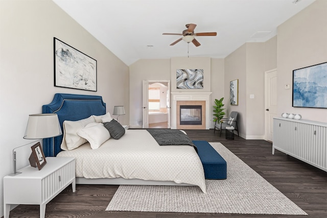 bedroom with a tiled fireplace, ceiling fan, and dark wood-type flooring