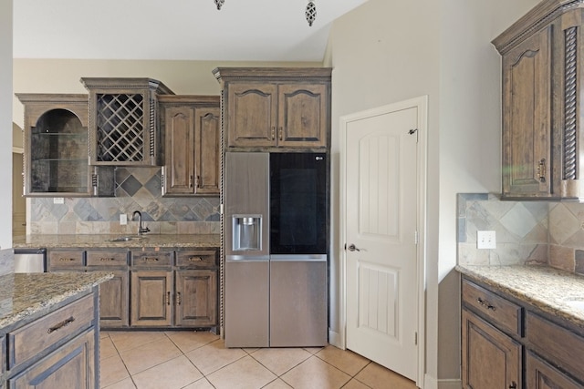 kitchen with sink, light stone counters, refrigerator with ice dispenser, backsplash, and light tile patterned flooring