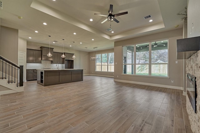 unfurnished living room featuring a raised ceiling, ceiling fan, a fireplace, and light hardwood / wood-style floors