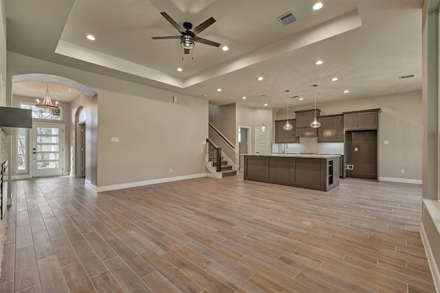 unfurnished living room featuring ceiling fan with notable chandelier, sink, and a tray ceiling