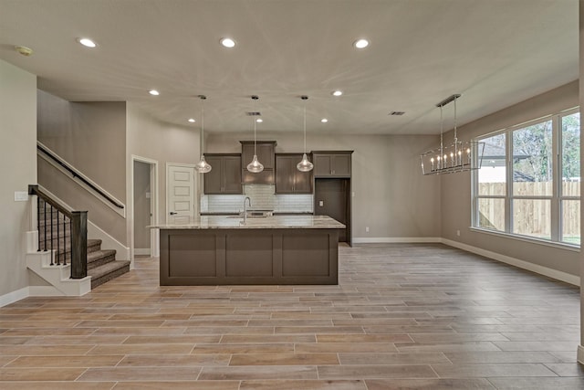 kitchen with light stone countertops, pendant lighting, a center island with sink, and sink