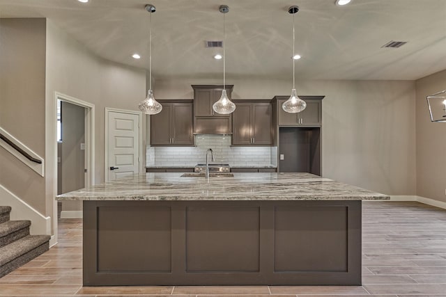 kitchen with sink, light stone counters, decorative light fixtures, a kitchen island with sink, and light wood-type flooring