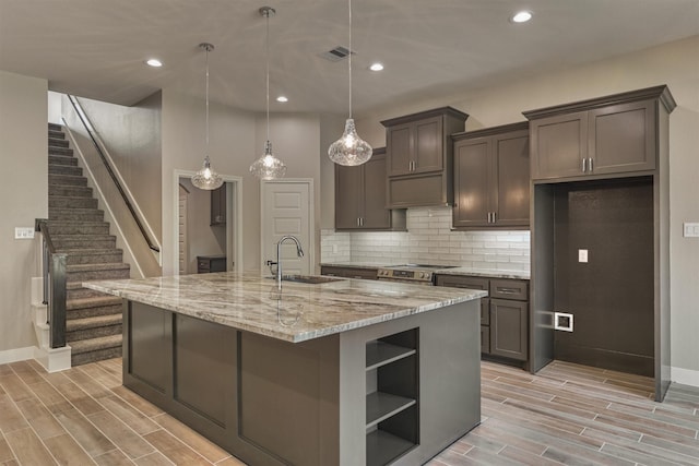 kitchen with light stone countertops, stainless steel electric stove, a kitchen island with sink, sink, and decorative light fixtures