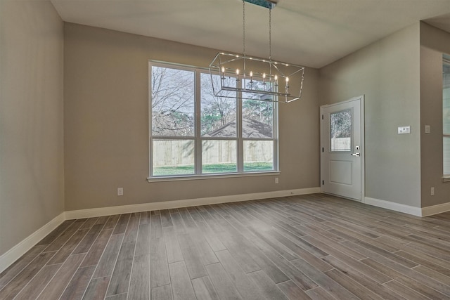 unfurnished dining area with a wealth of natural light, a chandelier, and wood-type flooring