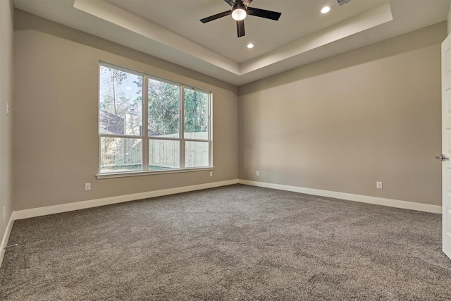 empty room featuring a tray ceiling, ceiling fan, and carpet floors