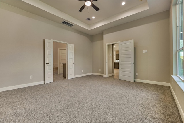 unfurnished bedroom featuring carpet flooring, a tray ceiling, and ceiling fan