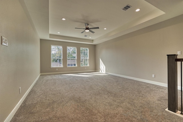 unfurnished room with a raised ceiling, ceiling fan, and carpet