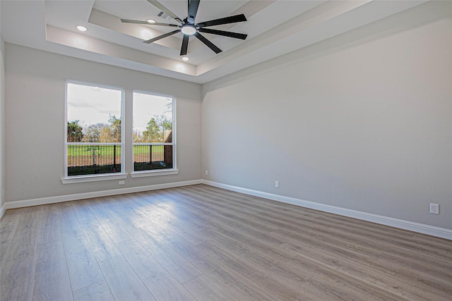 empty room featuring light wood-type flooring, a raised ceiling, and ceiling fan