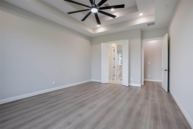 unfurnished bedroom featuring ceiling fan, light hardwood / wood-style floors, and a tray ceiling