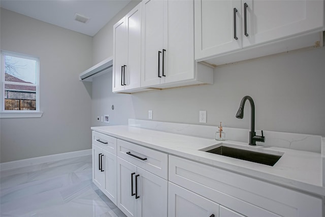 kitchen with white cabinetry, light stone counters, and sink