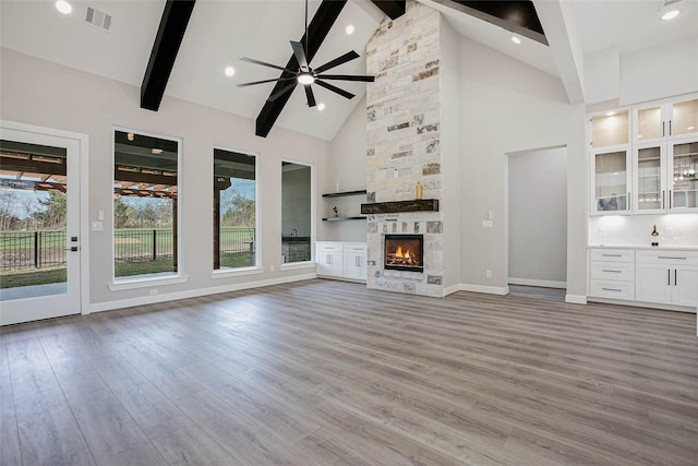 unfurnished living room featuring beamed ceiling, light hardwood / wood-style flooring, high vaulted ceiling, and a fireplace