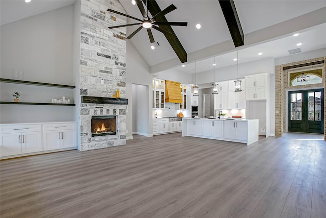 unfurnished living room featuring beamed ceiling, a stone fireplace, light wood-type flooring, and high vaulted ceiling