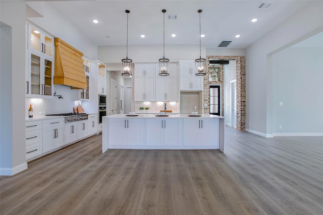 kitchen with backsplash, stainless steel appliances, a kitchen island with sink, white cabinetry, and hanging light fixtures