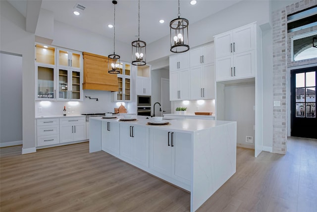 kitchen featuring built in microwave, pendant lighting, white cabinets, light hardwood / wood-style floors, and an island with sink