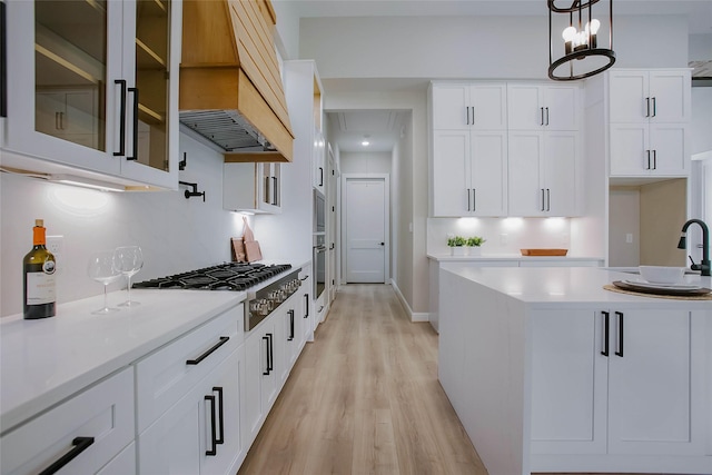 kitchen with pendant lighting, premium range hood, white cabinets, light wood-type flooring, and stainless steel appliances