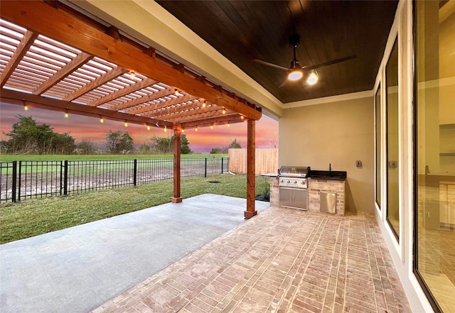 patio terrace at dusk with a pergola, grilling area, a lawn, and an outdoor kitchen