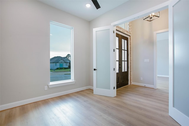 unfurnished room with french doors, a chandelier, and light hardwood / wood-style flooring