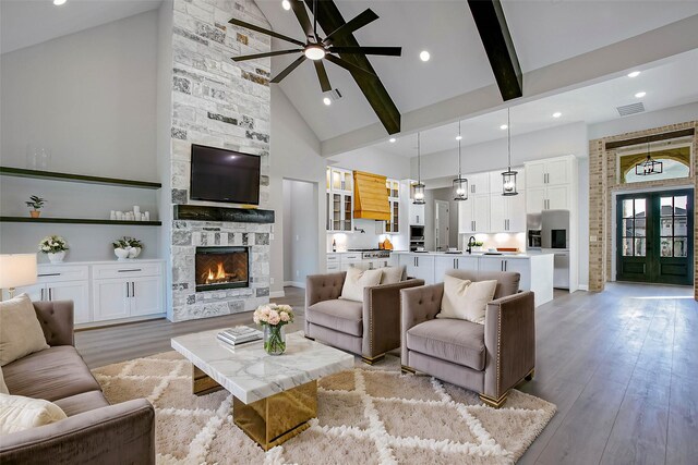 living room featuring beam ceiling, ceiling fan, a stone fireplace, high vaulted ceiling, and light wood-type flooring