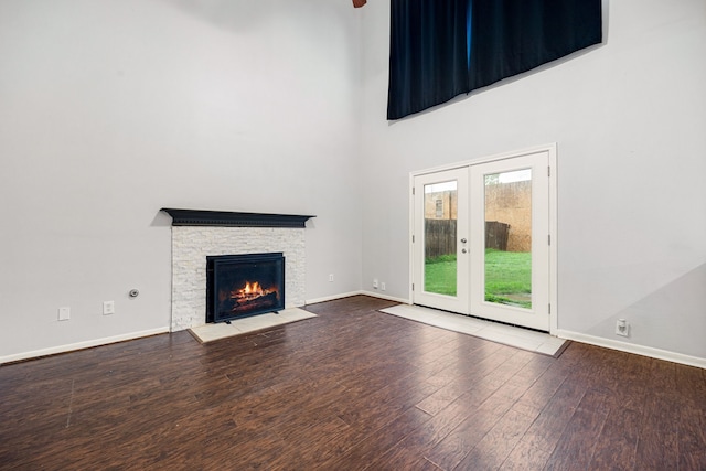 unfurnished living room featuring wood-type flooring, french doors, a stone fireplace, and a high ceiling