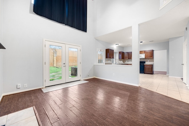 unfurnished living room with french doors, light hardwood / wood-style floors, and a high ceiling