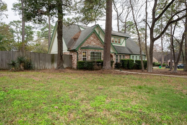 view of front facade with brick siding, a shingled roof, a front lawn, and fence