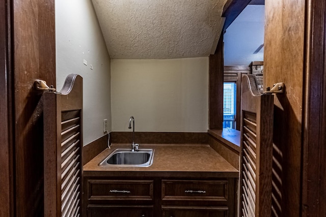 bar with a sink, lofted ceiling, and a textured ceiling