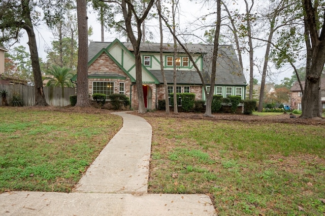 tudor home with a front yard, fence, and brick siding