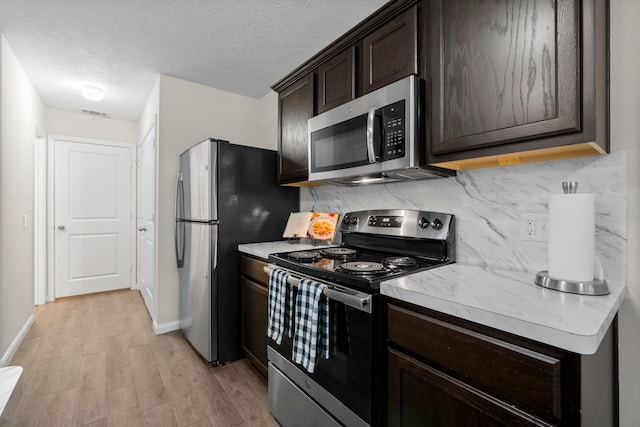 kitchen featuring backsplash, a textured ceiling, appliances with stainless steel finishes, dark brown cabinets, and light hardwood / wood-style floors