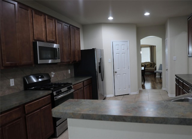 kitchen with dark brown cabinetry, sink, backsplash, light tile patterned floors, and appliances with stainless steel finishes
