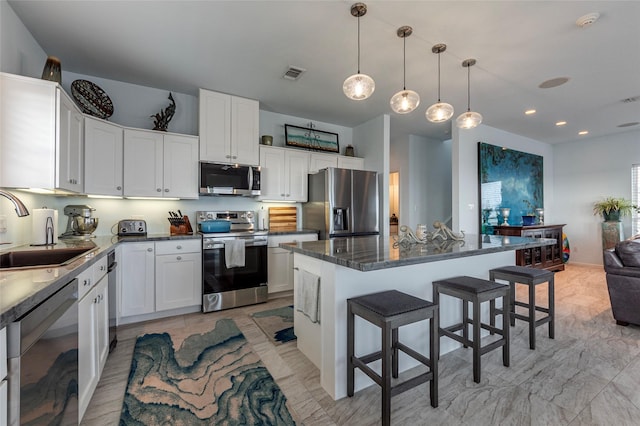 kitchen with visible vents, a kitchen bar, stainless steel appliances, a kitchen island, and a sink