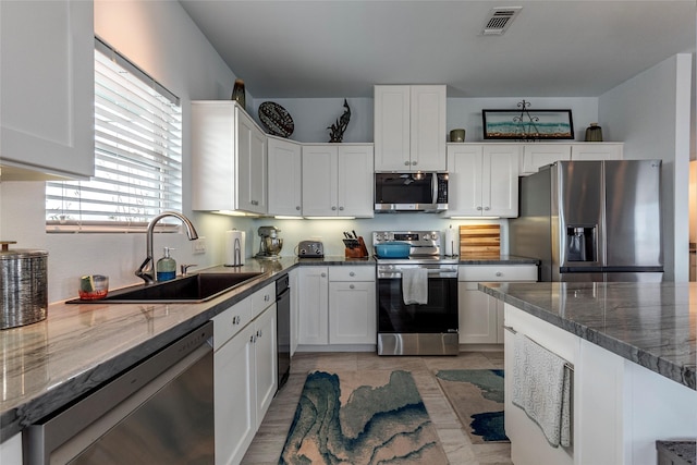 kitchen featuring dark stone counters, white cabinetry, sink, and stainless steel appliances