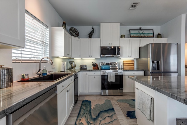 kitchen with white cabinetry, dark stone counters, a sink, visible vents, and appliances with stainless steel finishes