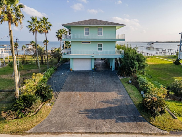 raised beach house featuring a carport, a water view, a balcony, a front lawn, and a garage