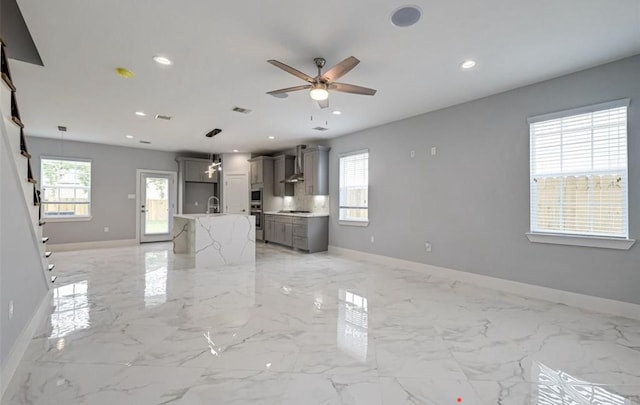 unfurnished living room featuring ceiling fan, sink, and a healthy amount of sunlight