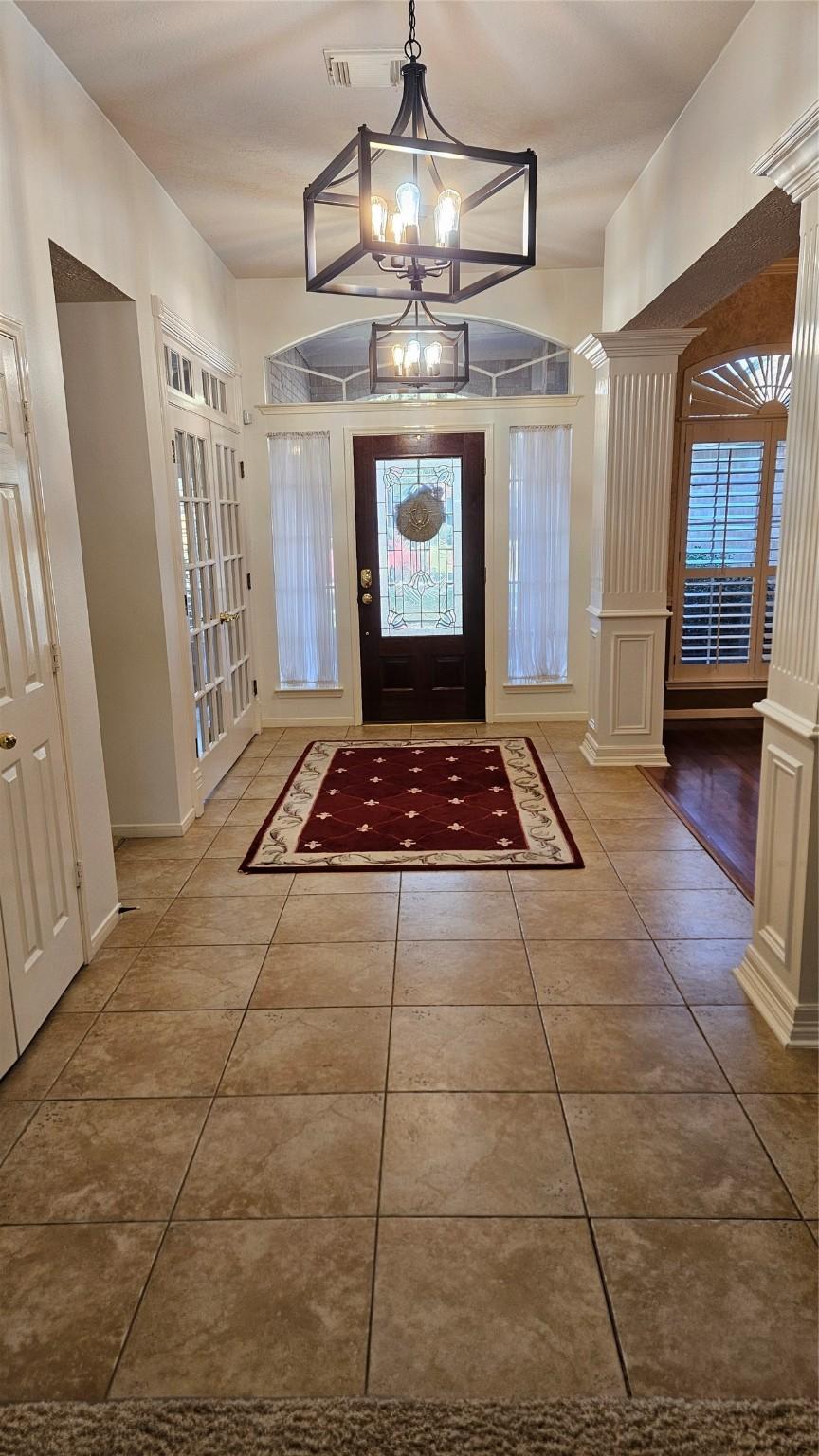 tiled entryway featuring decorative columns, a healthy amount of sunlight, and a chandelier