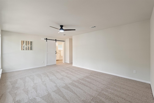 empty room with ceiling fan, a barn door, and light colored carpet