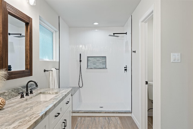 bathroom with hardwood / wood-style floors, vanity, toilet, and tiled shower