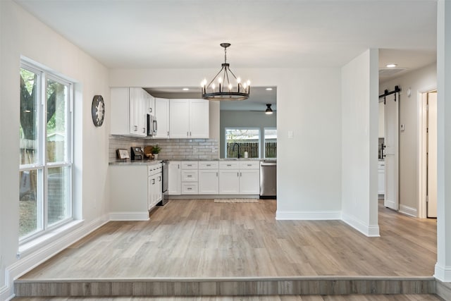 kitchen featuring white cabinetry, hanging light fixtures, stainless steel appliances, a barn door, and backsplash