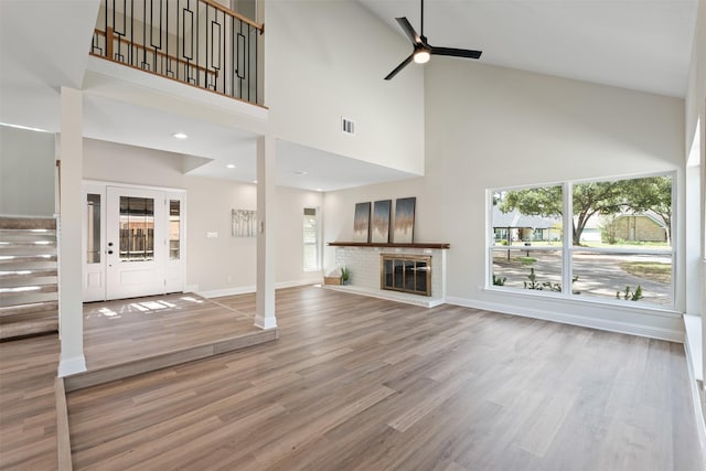 unfurnished living room featuring a high ceiling, a brick fireplace, a wealth of natural light, and wood-type flooring