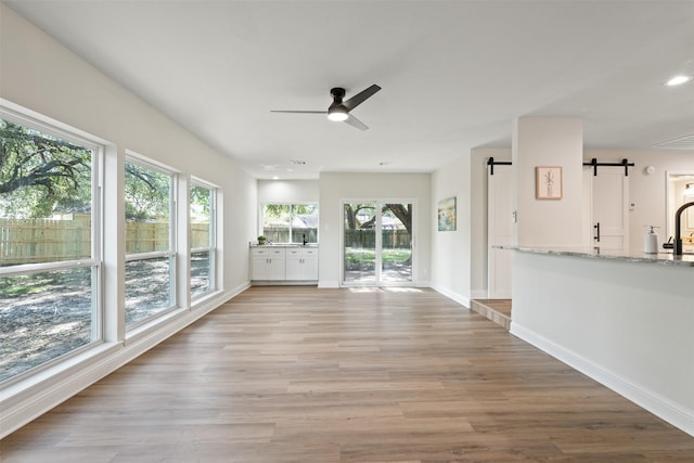 unfurnished living room with ceiling fan, a barn door, and light hardwood / wood-style flooring