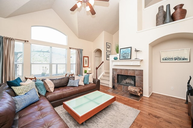 living room featuring a tile fireplace, ceiling fan, high vaulted ceiling, and wood-type flooring