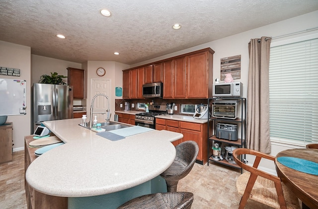 kitchen featuring appliances with stainless steel finishes, a textured ceiling, a center island with sink, and sink