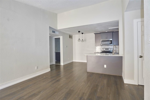 kitchen with dark hardwood / wood-style floors, kitchen peninsula, a textured ceiling, decorative light fixtures, and appliances with stainless steel finishes