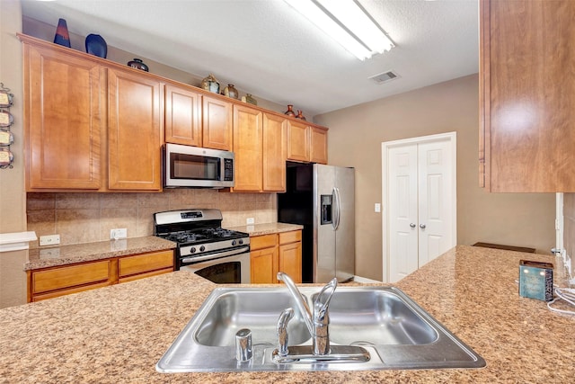 kitchen featuring appliances with stainless steel finishes, a textured ceiling, tasteful backsplash, and sink