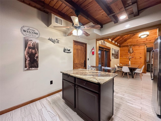 kitchen with stainless steel refrigerator, ceiling fan, light stone countertops, light hardwood / wood-style flooring, and wooden walls