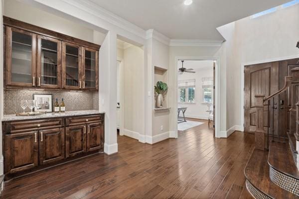 bar featuring backsplash, dark hardwood / wood-style flooring, light stone counters, dark brown cabinets, and crown molding